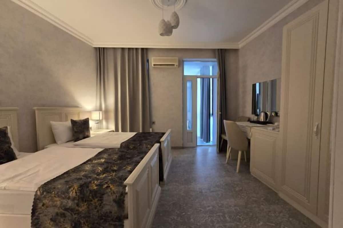A hotel room with two beds, a desk, a chair, a mirror, and a view of the outside.