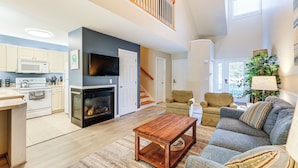 A modern kitchen with white cabinets, a microwave, and a fireplace. There is a dining area with a wooden table and a sofa. A staircase leads to an upper level. - 2 Mi to Bethany Beach Boardwalk! Townhome w/ Pool (Frankford)