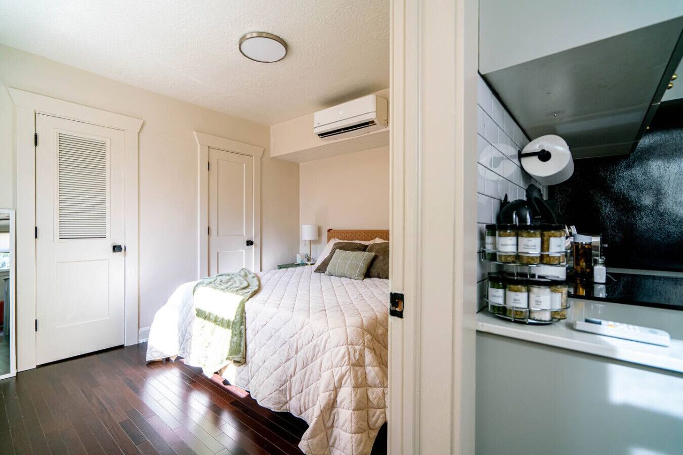 Un dormitorio con una cama, una mesita de noche, una lámpara y una estantería con frascos.