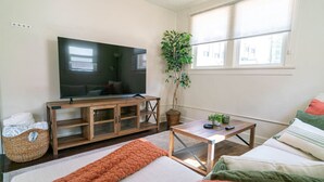A living room with a TV, wooden cabinet, sofa, and a potted plant. - Relaxing & Central SLC Apt near Trolley Square (Salt Lake City)