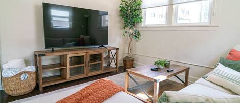 Una sala de estar con televisor, aparador de madera, sofá y planta en maceta.