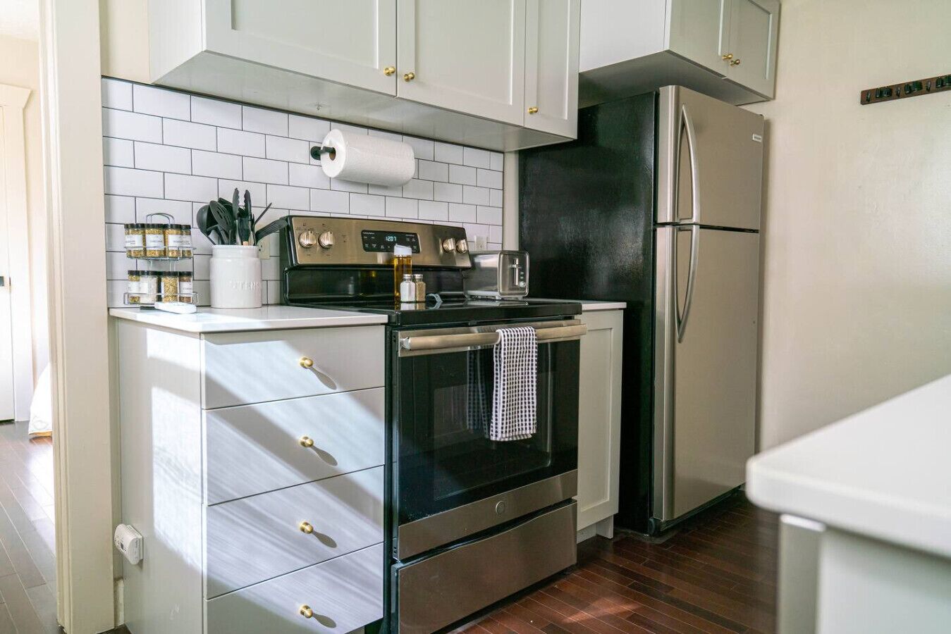 A compact kitchen with white cabinets, a black oven, a stainless steel refrigerator, and a tiled backsplash.