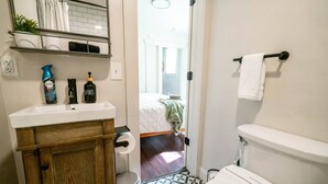 A bathroom with a white sink, a toilet, and a shower area. There is a towel rack with a towel hanging on it, and a small trash bin next to the sink. - Relaxing & Central SLC Apt near Trolley Square (Salt Lake City)