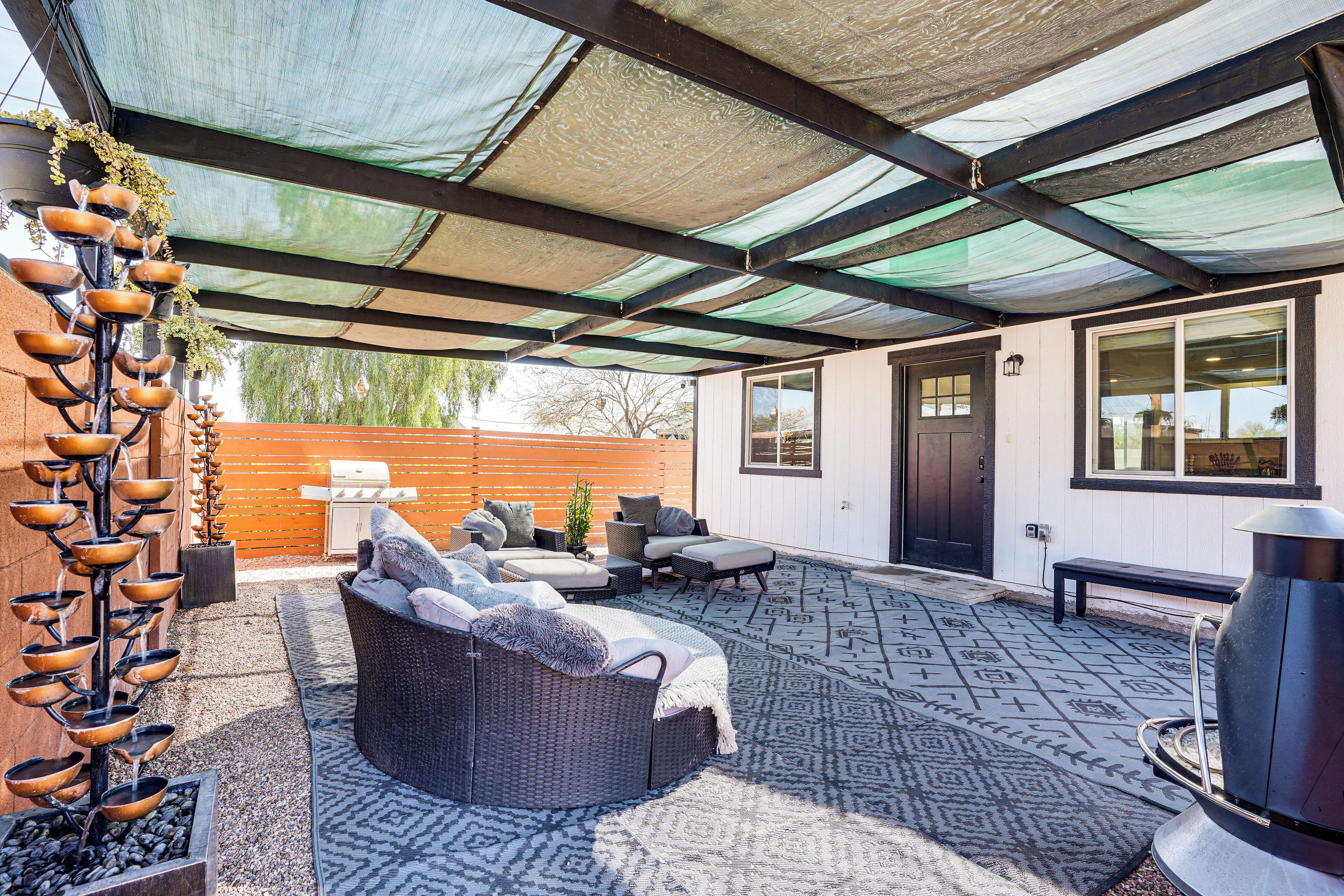 A covered patio area with outdoor seating, a barbecue grill, and a decorative water feature.
