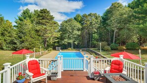 Une terrasse avec une piscine, des chaises rouges et des parasols.