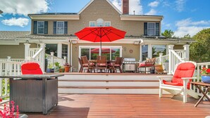 Une terrasse en bois avec des meubles d’extérieur, un barbecue et un grand parasol rouge.