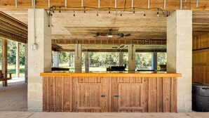 Zona de bar con barra de madera, ventilador de techo, pilares de concreto y vistas al exterior.
