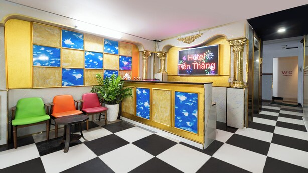A hotel reception area with a checkered floor, a reception desk, and three chairs in green, orange, and red. - Collection O District Tan Phu - Tien Thang Hotel  (Ho Chi Minh City)