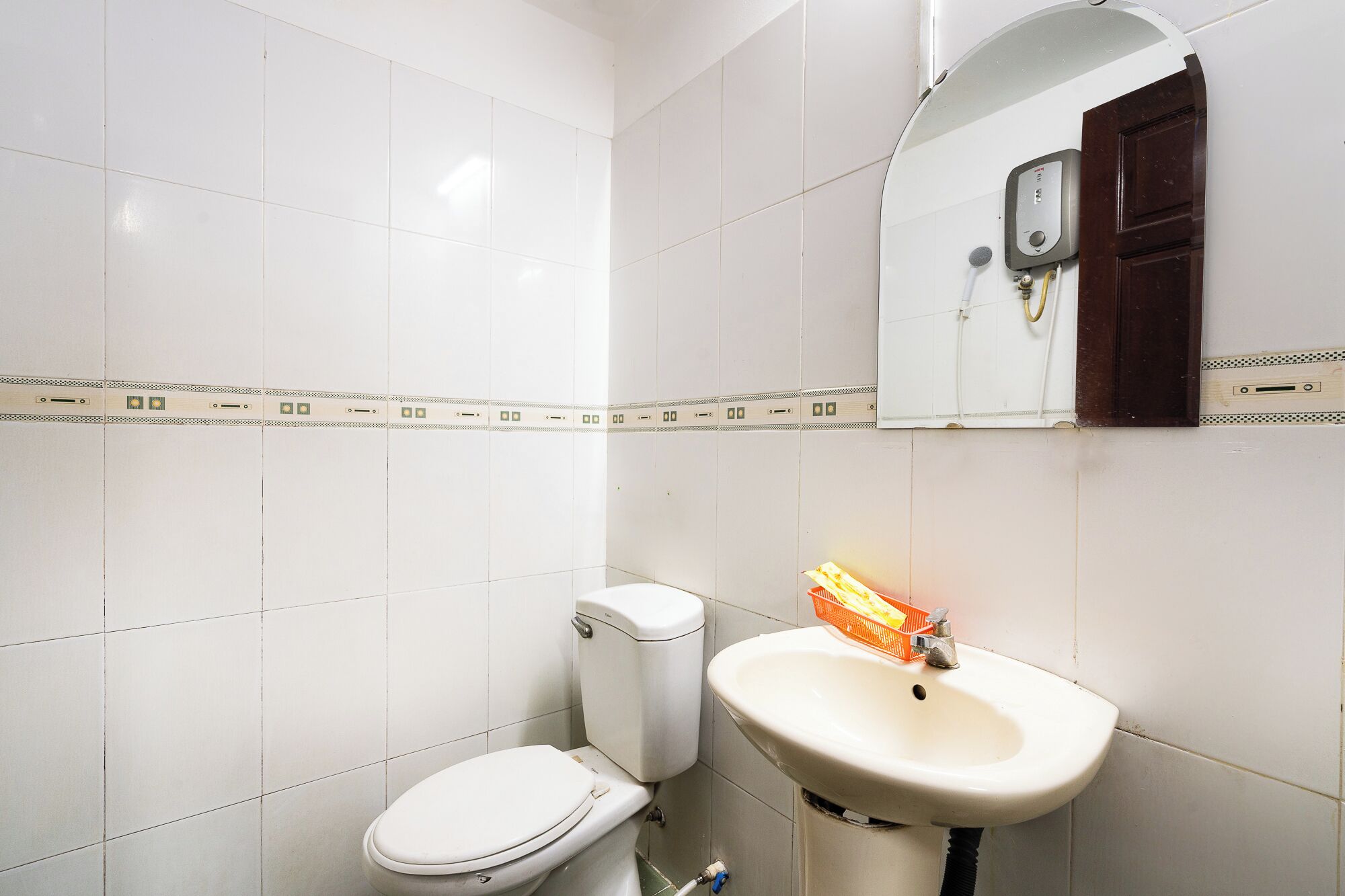 Een badkamer met witte tegels, een toilet, een wastafel en een spiegel.
