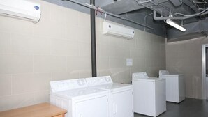 A laundry room with three white washers and dryers, a wooden bench, and exposed ductwork. - Lancaster Ho Chi Minh Serviced Apartment Official (Ho Chi Minh City)