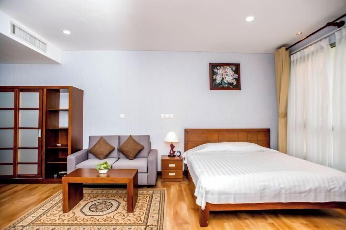 A bedroom with a bed, a sofa, a nightstand, a lamp, a wooden wardrobe, and a painting on the wall.