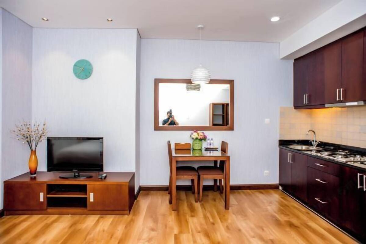 Un espace de vie compact comprenant une télévision, une table à manger, des chaises, une horloge, un miroir et des meubles en bois.