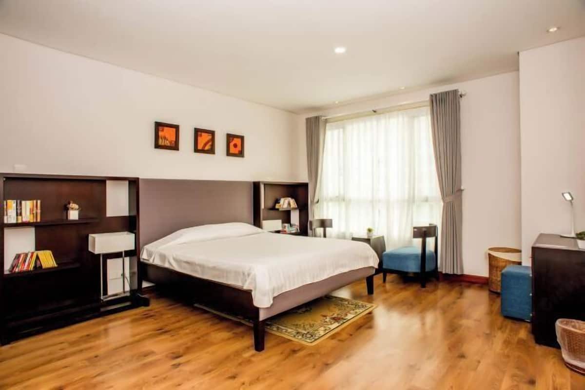 Une chambre à coucher avec un lit, des tables de chevet, un bureau, une chaise et une fenêtre avec des rideaux.