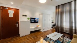 A modern hotel room with a wooden floor, a TV on a stand, a white cabinet, and a sliding door. - Lancaster Ho Chi Minh Serviced Apartment Official (Ho Chi Minh City)