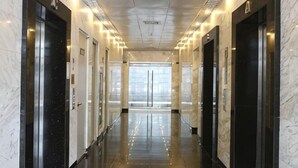 A corridor with marble walls, black doors, and a reflective floor leading to a large window. - Lancaster Ho Chi Minh Serviced Apartment Official (Ho Chi Minh City)