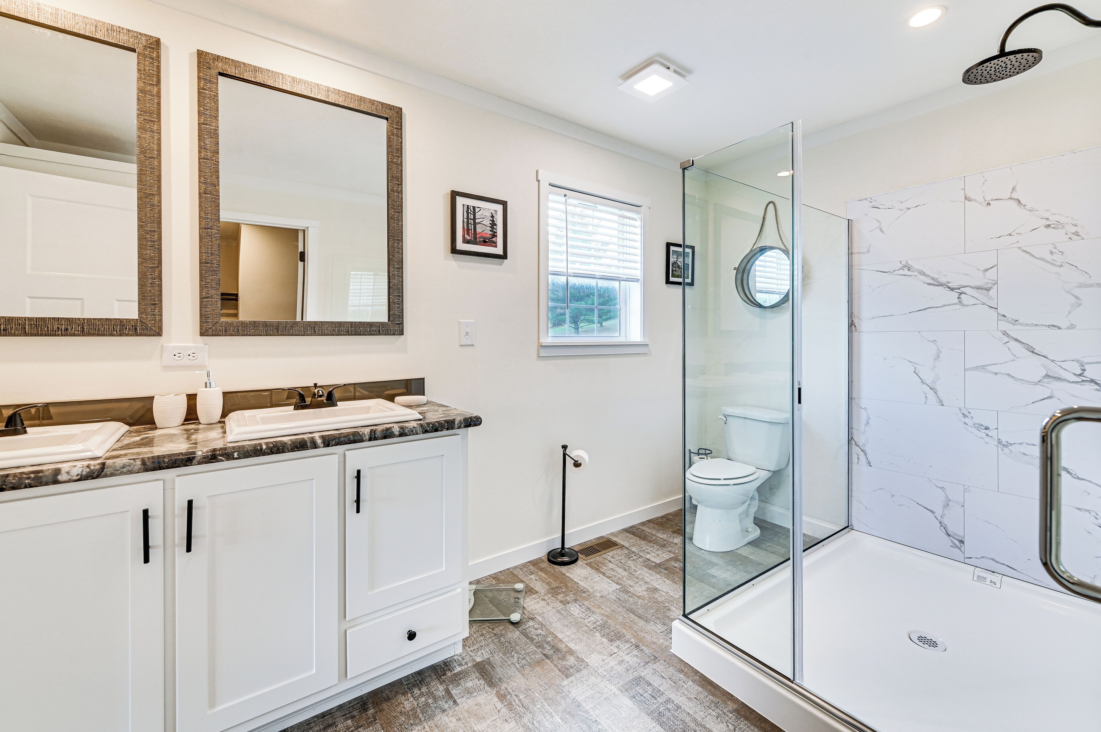 Un baño con cabina de ducha de vidrio, tocador doble y pared de ducha con azulejos de mármol.