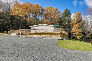 Une cabane dotée d’une terrasse en bois, d’un porche couvert et d’une allée gravillonnée.