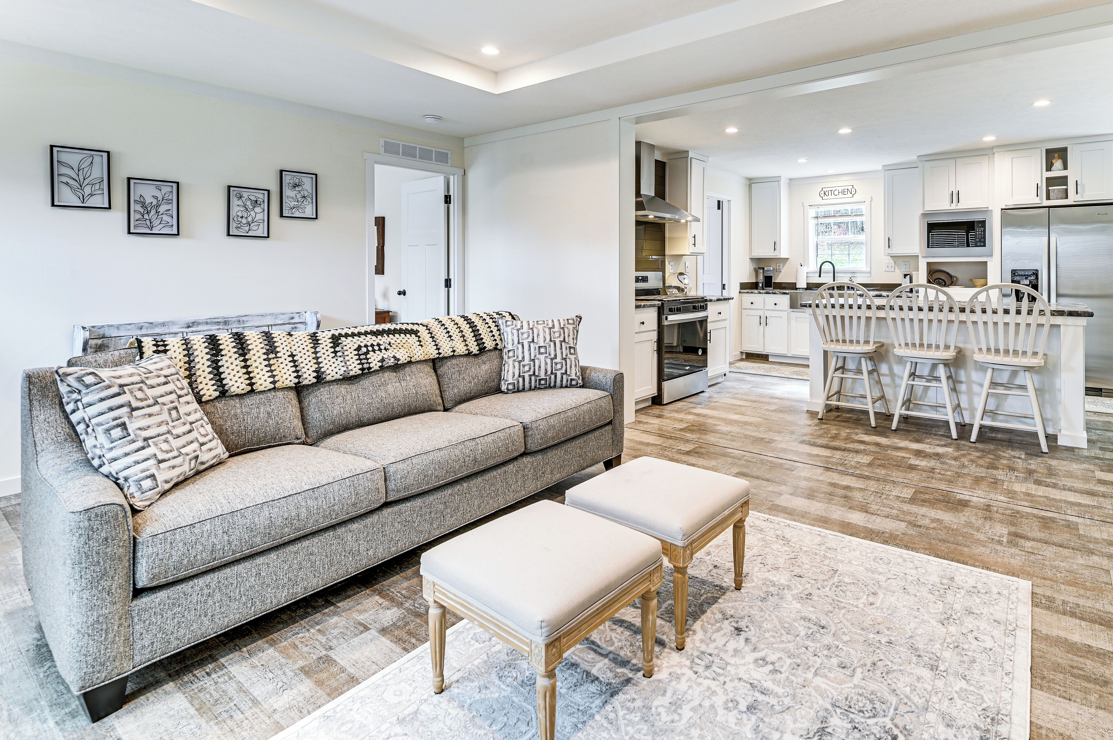 A modern living room with a grey sofa, a coffee table, and a kitchen area with white cabinets and stainless steel appliances.