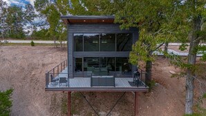 A modern two-story cabin with a deck, large windows, and a view of the surrounding landscape.