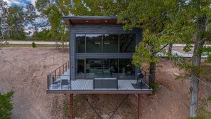 A modern two-story cabin with a deck, large windows, and a view of the surrounding landscape.