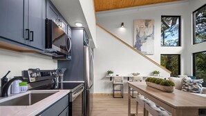A modern kitchen with stainless steel appliances, a wooden dining table, and a staircase leading to an upper level.