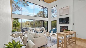 A spacious living area with large windows, a ceiling fan, a fireplace, and a dining area.