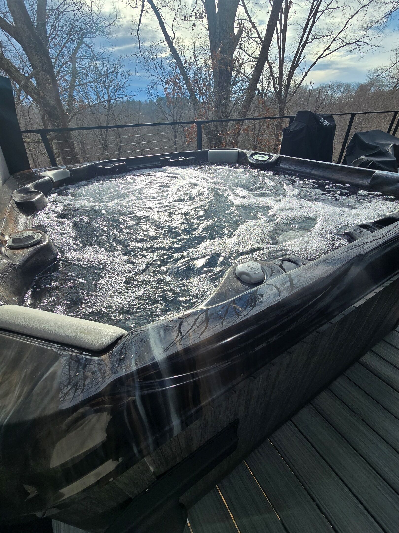 A hot tub on a wooden deck with a view of trees and sky.
