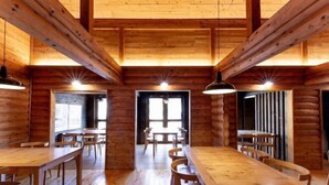 A spacious wooden cabin with multiple dining tables and chairs, large windows, and a high ceiling with exposed beams. - Hanarenoyado Hanagokoro　ASO (Minamioguni)