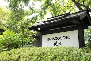 Ein Schild mit der Aufschrift 'HANAGOCORO', umgeben von Grünpflanzen.