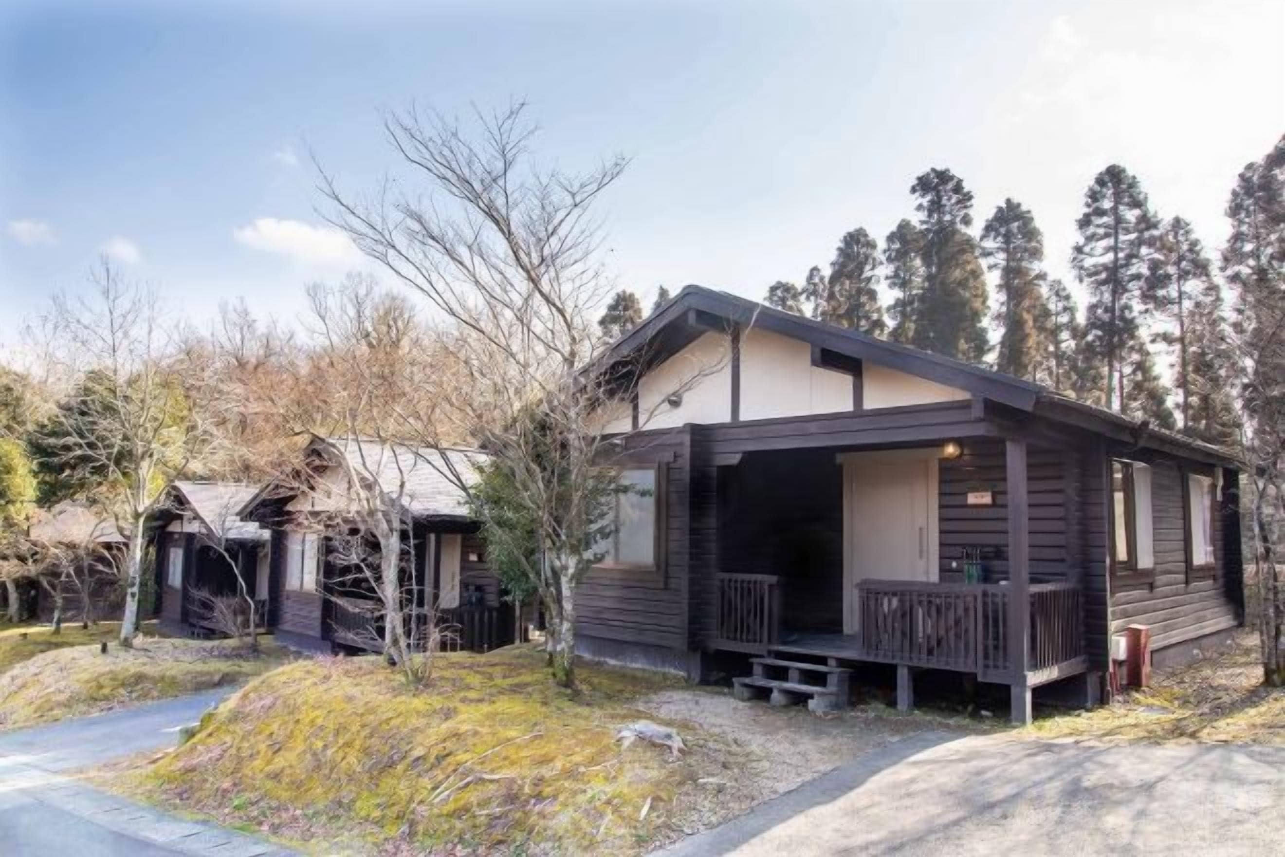 A single-story wooden cabin with a porch, surrounded by trees.