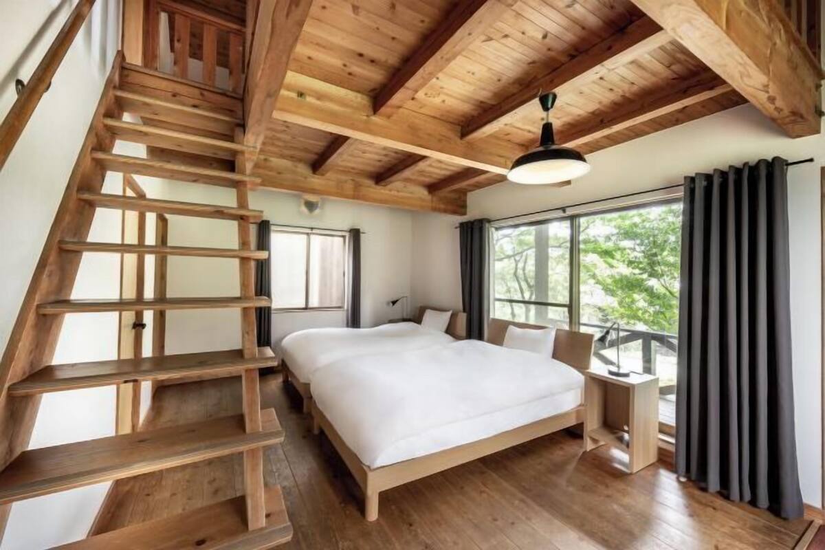 Una camera da letto con una scala in legno, un letto grande, un comodino e una finestra con tende.