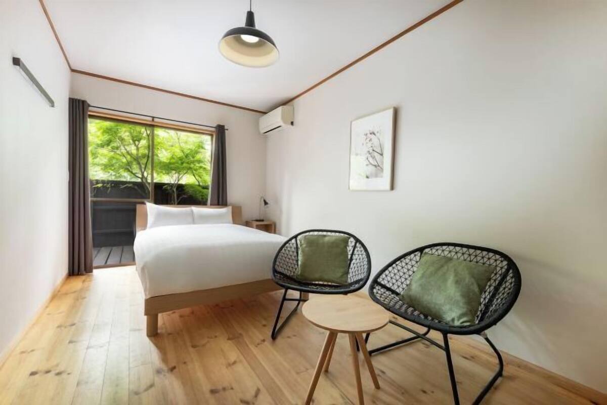 Una camera da letto con un letto, due poltrone, un tavolino, una finestra vista e una lampada a soffitto.