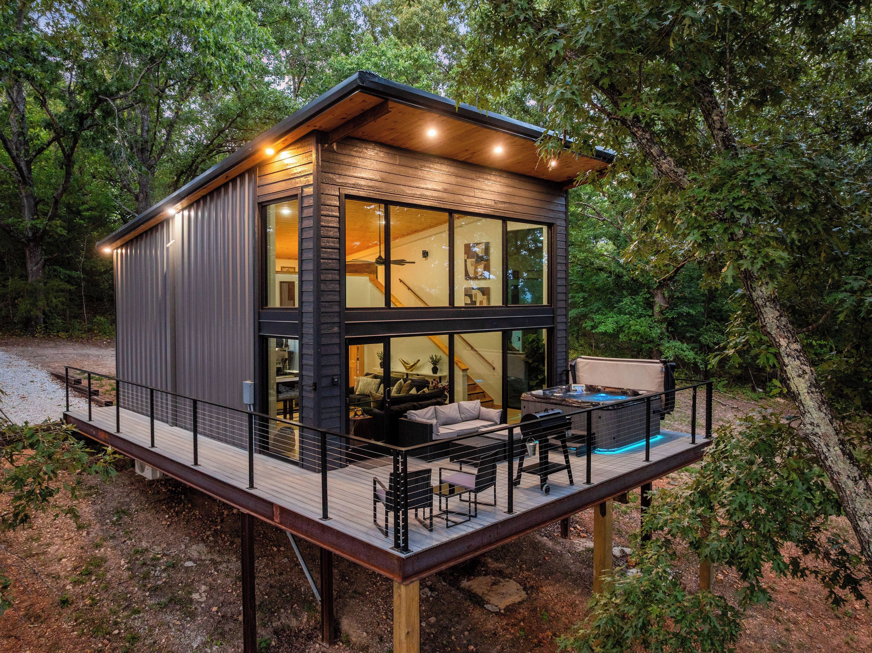 A modern cabin with a deck, large windows, and a hot tub.