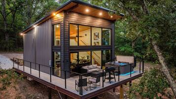 A modern cabin with a deck, large windows, and a hot tub.