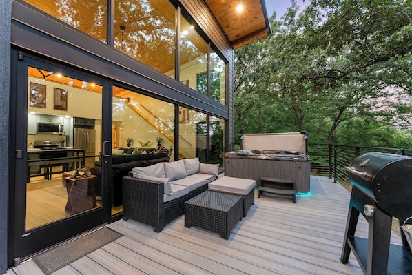 A modern outdoor deck with a hot tub, grill, and wicker furniture.