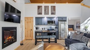 Una sala de estar moderna con chimenea, un sofá, una mesa de centro y una zona de cocina con armarios y electrodomésticos.
