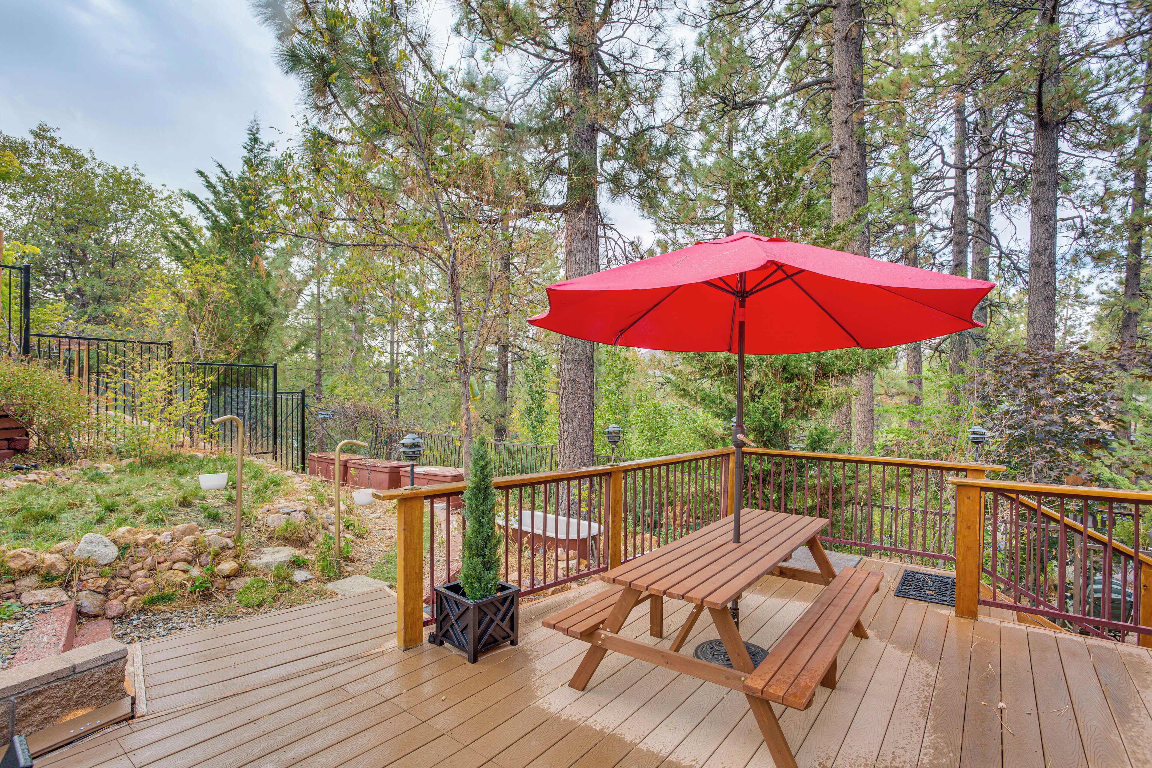 Eine Holzterrasse mit einem roten Sonnenschirm, umgeben von Bäumen und einem Steinweg.