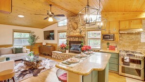 A spacious kitchen with a stone fireplace, wooden ceiling, and modern appliances. - 3 Mi to Snow Summit: Charming Home w/ Fenced Yard (Big Bear Lake)