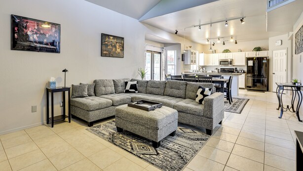 A spacious living room with a sectional sofa, ottoman, and a coffee table. There is a kitchen area with modern appliances and a dining table. - Labor Day Weekend Special: Flexible Check-In/Out! (Phoenix)