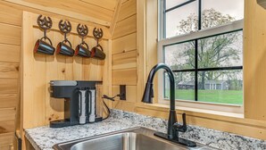 A kitchen with a stainless steel sink, wooden cabinets, a coffee maker, and a window with a view of a green landscape. - 5 Mi to Wine Trails: Finger Lakes Tiny Home (Ovid)