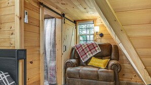 A cozy room with a brown leather armchair, a plaid throw blanket, and a yellow pillow. - 5 Mi to Wine Trails: Finger Lakes Tiny Home (Ovid)
