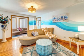 Un salón con sofá, otomana redonda y una pared con diseño de olas.