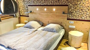 A bed with a checkered bedspread, two pillows, a headboard, and a wooden wall with a stone pattern. - Beautiful apartment for 2 people with WIFI, TV, balcony and pets allowed (Thurmbach)