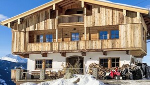 A two-story wooden chalet with a balcony, large windows, and a mountain backdrop. - Beautiful apartment for 2 people with WIFI, TV, balcony and pets allowed (Thurmbach)