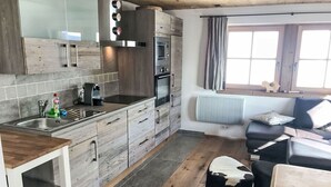 Une cuisine moderne équipée d’un four encastré, d’un évier et d’une machine à café. Il y a une fenêtre avec des rideaux et un radiateur au mur.