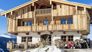 Een houten chalet met twee verdiepingen, een balkon, grote ramen en een berg op de achtergrond.
