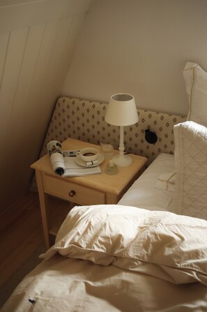 A small bedroom with a single bed, a nightstand with a lamp, a cup of coffee, and a newspaper.