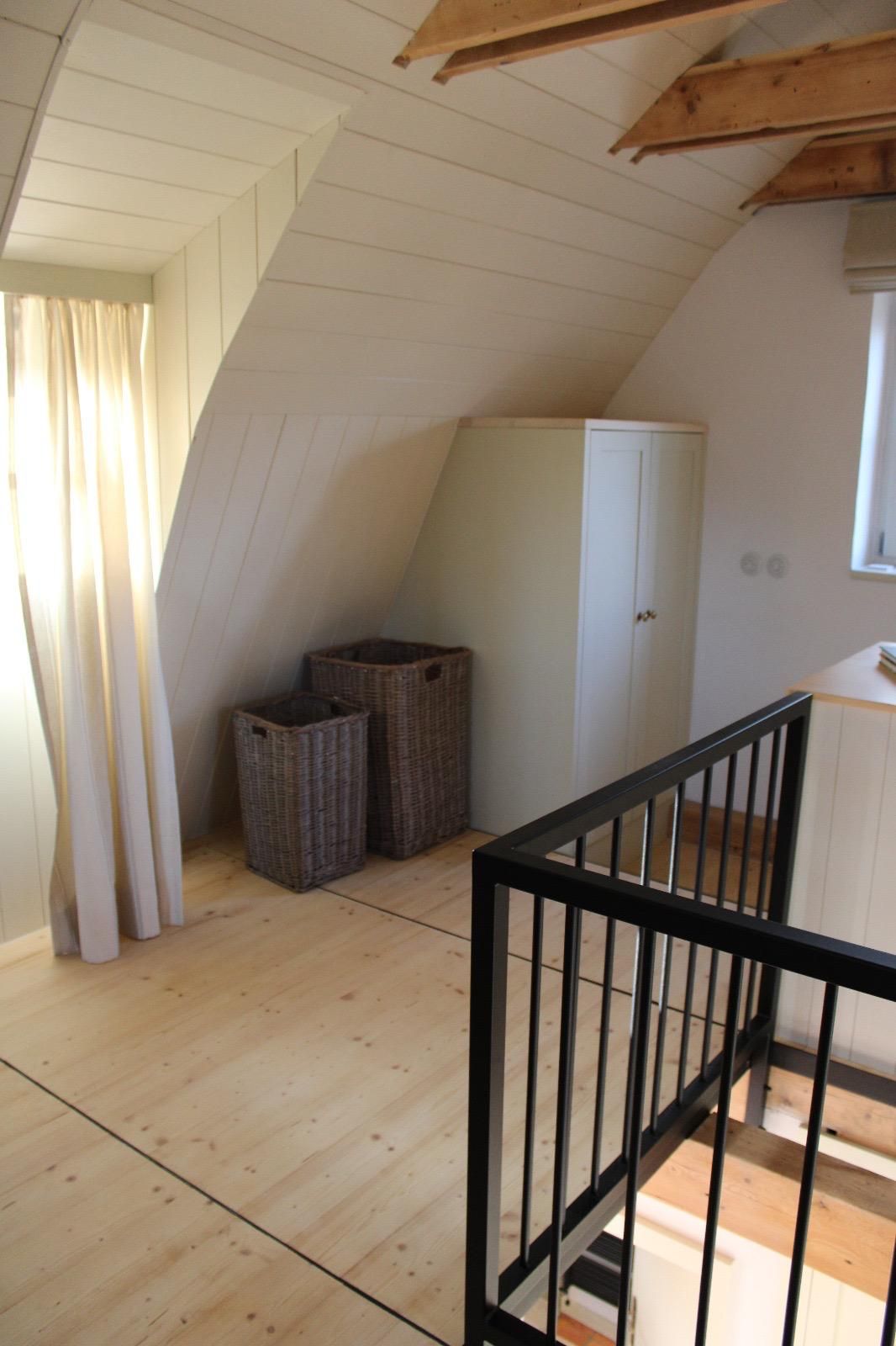 A room with a sloped ceiling, a wooden floor, a white wardrobe, and wicker baskets.