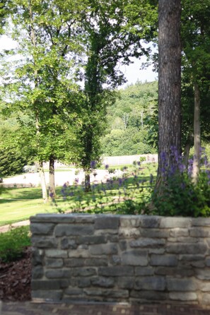 A stone wall, trees, and a grassy area with a fence in the background. - Peaceful Country Retreat – Restored 1910 Cottage near Milešovka (Bořislav)