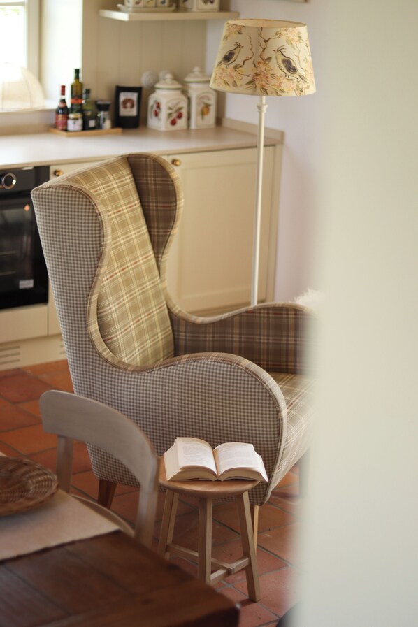 A chair with a plaid pattern, a small stool with an open book, and a lamp with a bird design.